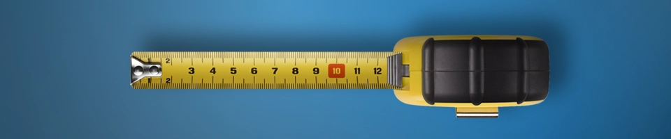 Un metro a nastro giallo è esteso su uno sfondo blu scuro. Il nastro mostra misurazioni in centimetri e millimetri. Il metro è visto dall’altro e si legge al massimo la misura dei 12 cm.