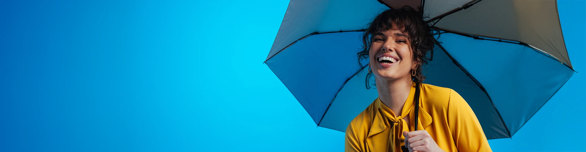 Giovane donna che ride e tiene un ombrello su uno sfondo blu