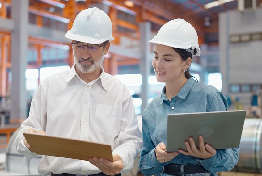 Un uomo e una donna con elmetto osservano dei documenti in un ambiente di lavoro