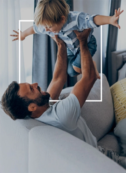 Uomo adulto solleva un bambino in aria nel soggiorno, in un momento di gioco