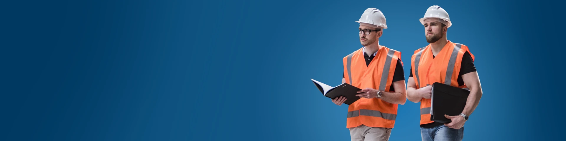 Due uomini in abiti da lavoro posano su uno sfondo blu uniforme. Entrambi indossano caschi protettivi bianchi e giubbotti di sicurezza arancioni ad alta visibilità con strisce catarifrangenti. L'uomo a sinistra ha la barba e tiene una cartellina nera sotto il braccio, mentre l'uomo a destra porta gli occhiali e tiene una cartellina nera tra le mani. Entrambi guardano verso la loro destra con espressione seria.