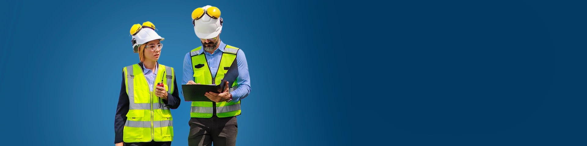 Due ingegneri, un uomo e una donna, in piedi fianco a fianco su uno sfondo blu solido. Entrambi indossano caschi bianchi con paraorecchie protettivi gialli e giubbotti di sicurezza giallo-verdi riflettenti. La donna, a sinistra, guarda verso l'alto con un'espressione pensierosa, tenendo una radio bidirezionale in mano. L'uomo, a destra, guarda in basso mentre scrive o esamina dei documenti su una cartellina nera. L'illuminazione è luminosa e uniforme.