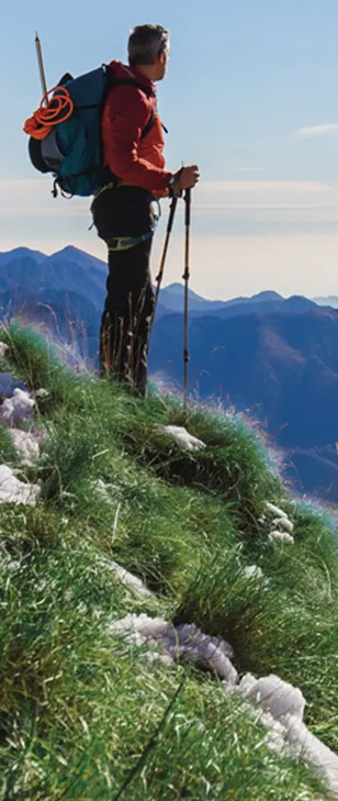 Uomo con zaino e bastone che ammira il panorama dalla vetta di una montagna.